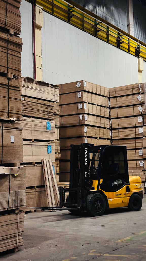 A yellow forklift organizes large stacks of cardboard boxes in a spacious warehouse.