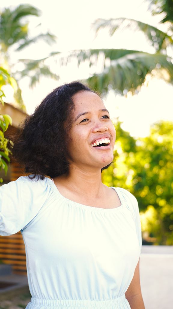 Cheerful woman with curly hair enjoying sunny day outdoors, surrounded by greenery.